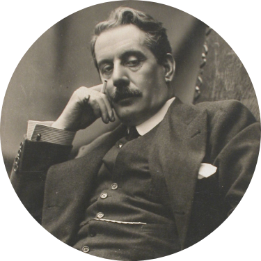 L'immagine d'epoca ritrae in primo piano Giacomo Puccini seduto, che guarda direttamente verso l'obiettivo con la testa poggiata sulla mano in cui tiene una sigaretta fra le dita.
