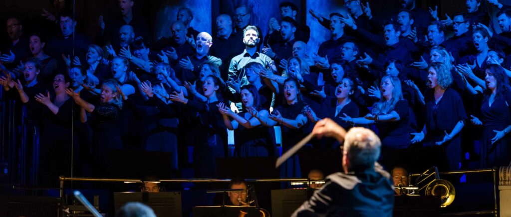 Scena dell'opera Turandot al Leeds Town Hall. Il tenore è illuminato da una potente luce bianca, mentre il coro, rimasto in ombra, affolla il palco.